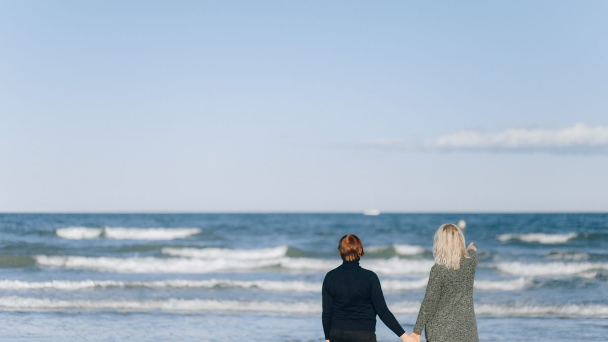 A romantic scene of a couple holding hands while enjoying a walk by the sea on a sunny day.